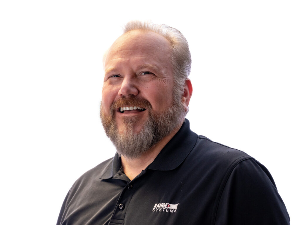 Close-up portrait of a smiling man with a gray beard wearing a black polo shirt, white background behind him.